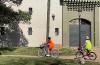 Dos niñas avanzan por un camino en bicicleta, una lleva un chaleco naranja y la otra niña, un chaleco verde refractario. Al fondo, se ve la puerta del Castillito del Parque Rodó. 