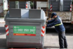 Fotografía de un contenedor de basura y un funcionario que lo mueve 