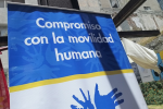 Fotografía con detalle de un cartel: sobre fondo azul con letras blancas dice "Compromiso con la movilidad humana"