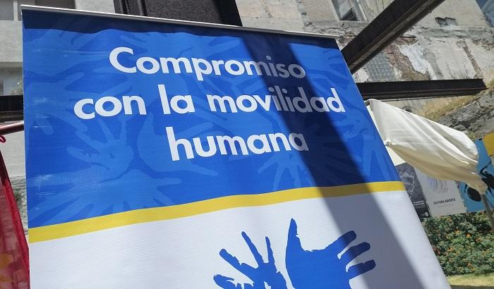 Fotografía con detalle de un cartel: sobre fondo azul con letras blancas dice "Compromiso con la movilidad humana"