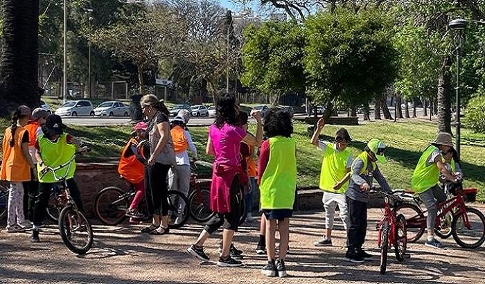 Grupo de niños y niñas reunidos junto a unas bicicletas. Visten chalecos con colores refractarios. 